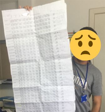Pessoa segura uma planilha de orçamento impressa em várias folhas coladas, maior que o próprio corpo